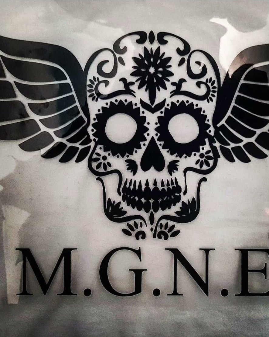 Heller Stoff mit schwarzem Totenkopf-Motiv mit Flügeln und Schriftzug M.G.N.E