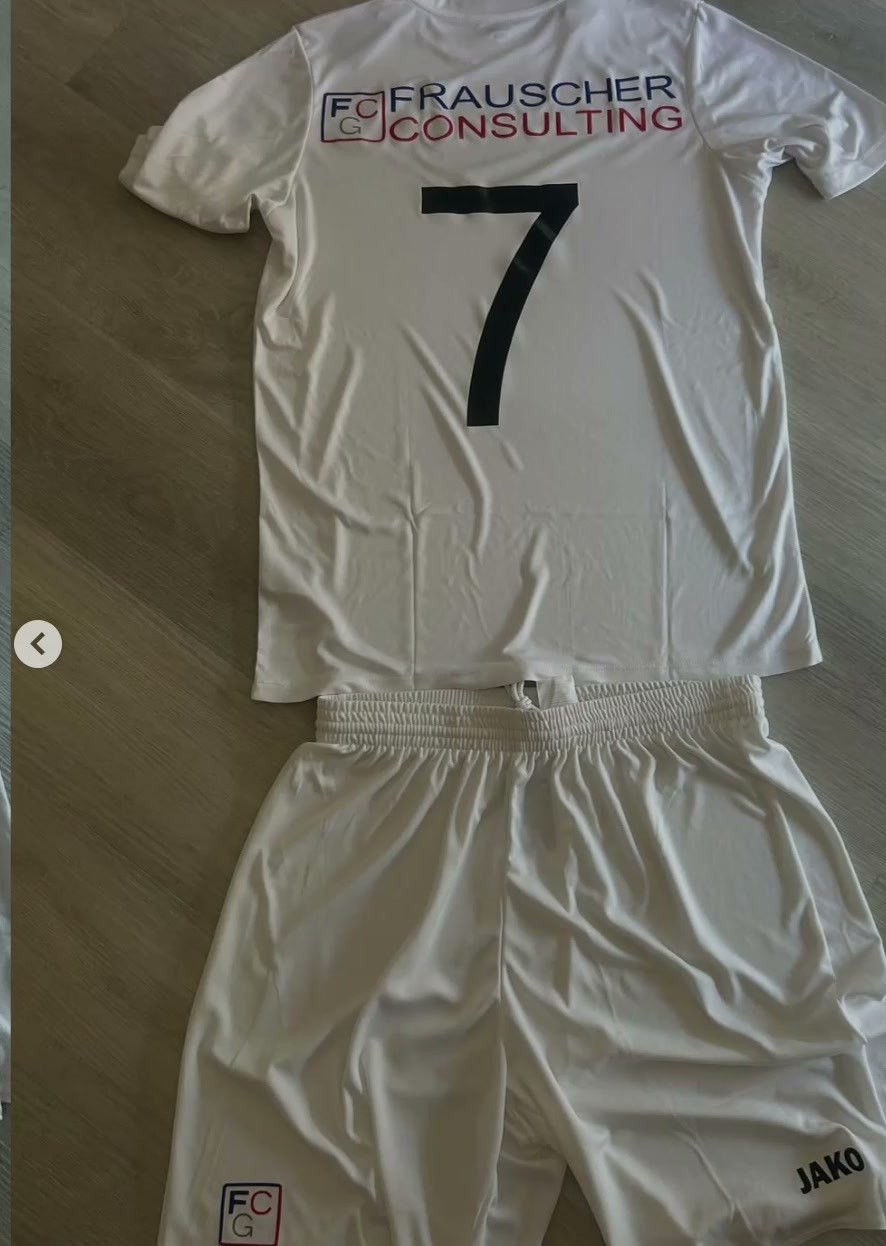 Weißes Fußballtrikot mit Sponsordruck und Nummer 7, dazu weiße Hose